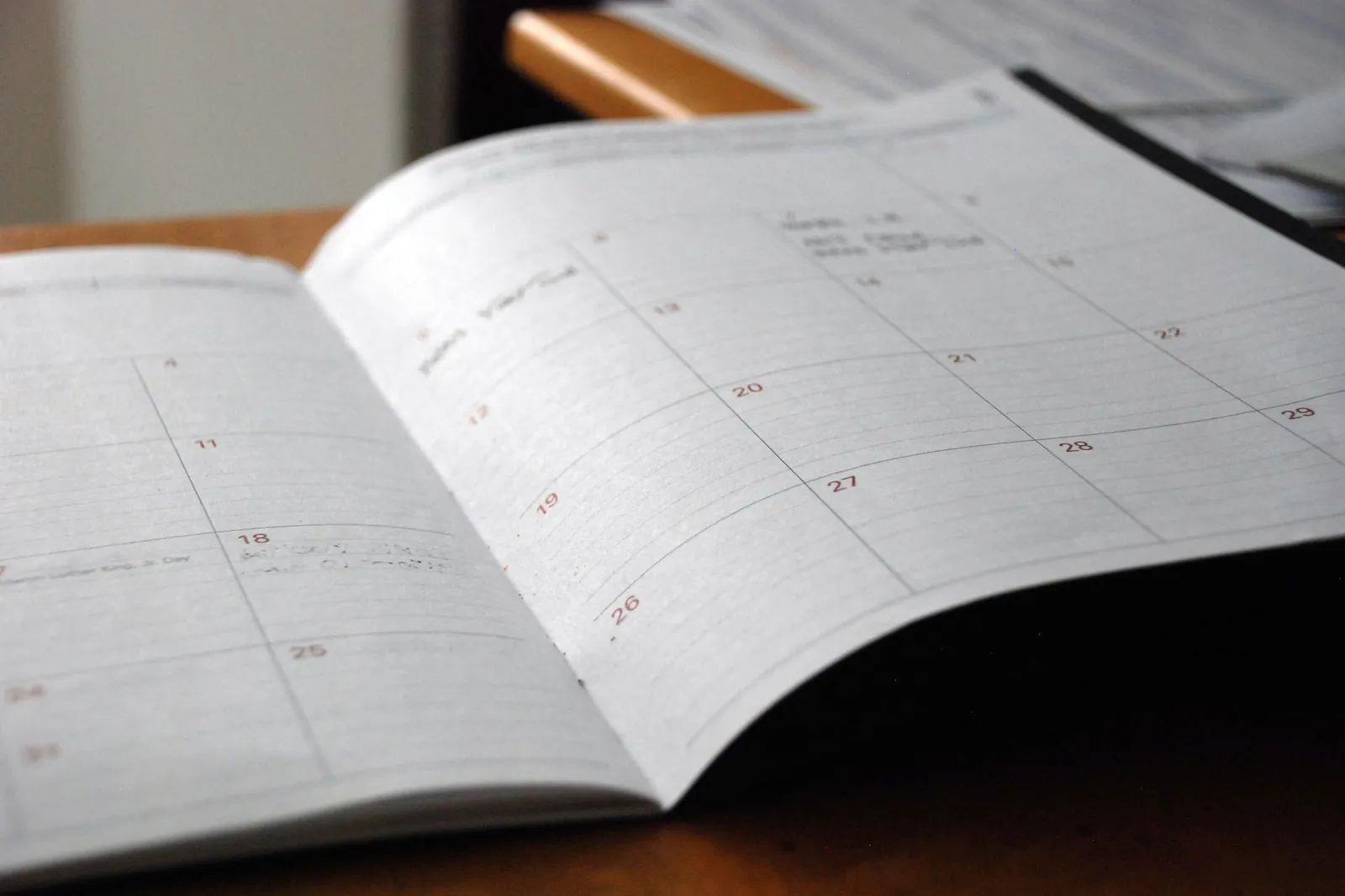Opengeslagen maandagenda op een houten tafel, met papieren op de achtergrond