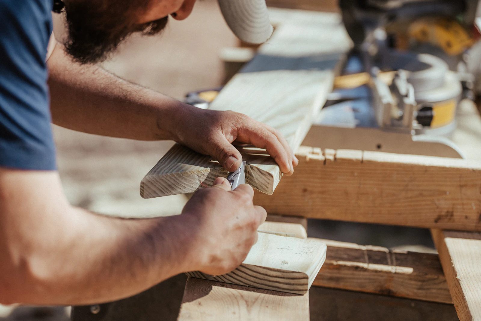 Man in een blauw shirt bewerkt een houten plank met handgereedschap op een werkbank