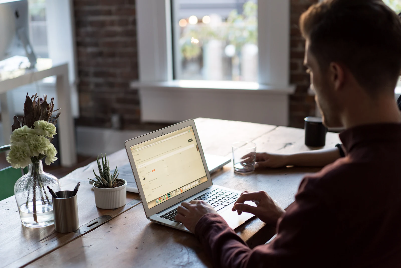 Man typt op een laptop aan een houten tafel bij het raam