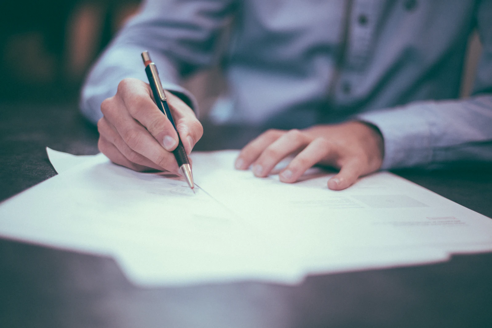 Man in lichtblauw overhemd zet een handtekening op papieren