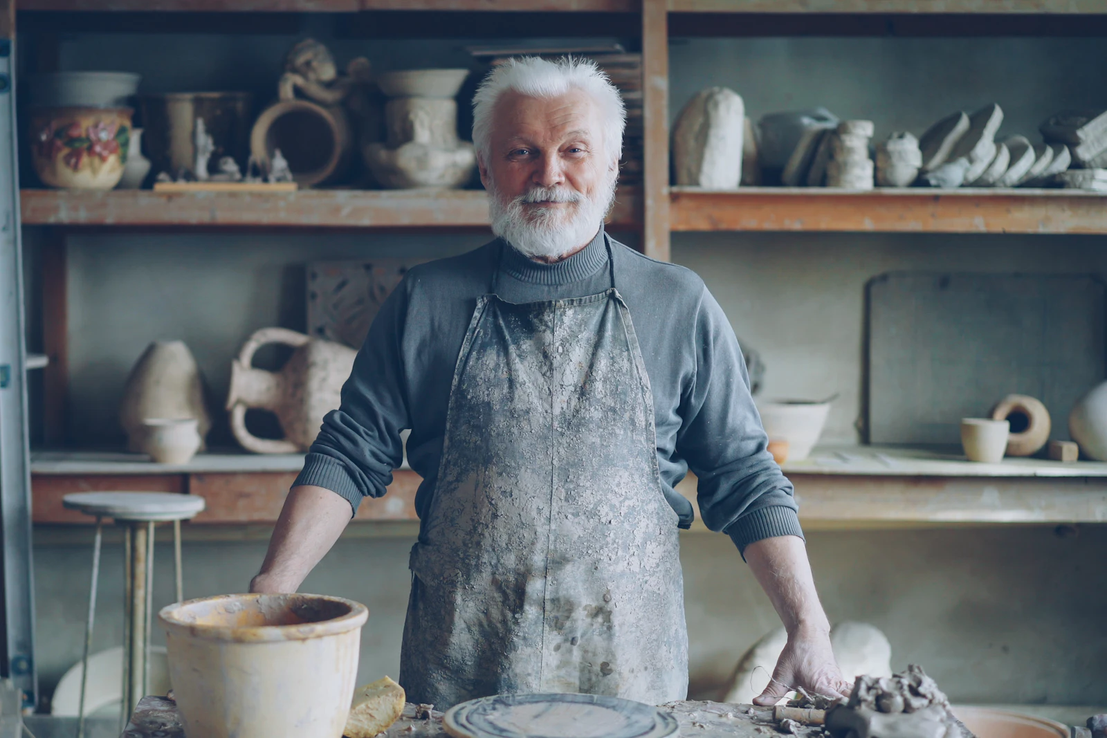 Oudere pottenbakker met grijze baard en schort in zijn atelier