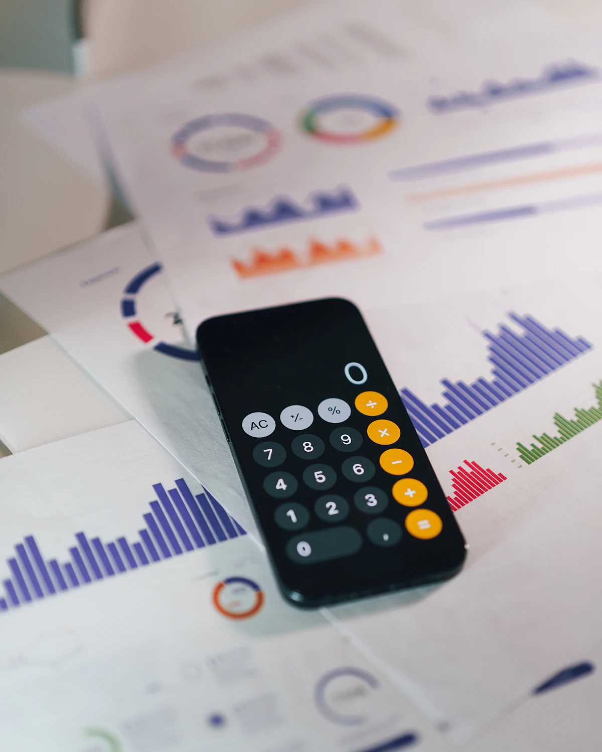 Telefoon met een rekenmachine-app op een stapel rapporten met staafdiagrammen